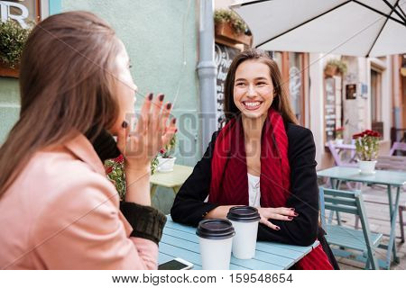 Two cheerful pretty young women talking and lauging in outdoor cafe