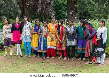 Nilgiri Hills India - October 25 2013: Colorful group of young Indian smiling college women posing in a row at the Ooty Botanical Garden. Bright colors of clothing against green background.