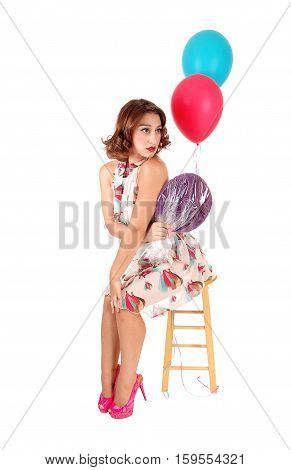 A beautiful young woman siting on a chair holding a lollypop and balloons isolated for white background.