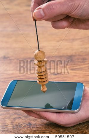 Hand with pendulum dowsing over smart phone to check its quality, dangerous influence or radiation