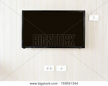 Blank lcd Flat screen television hanging at the planks wooden wall with copy space in living room or bedroom. White home electrical switch and plug outlet on a light brown or beige color wooden wall.