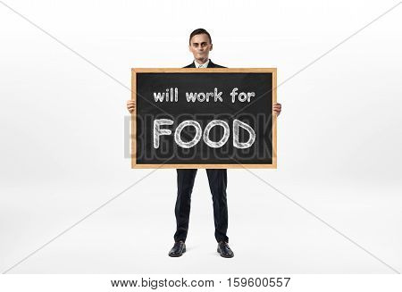 A businessman holding a blackboard with the words 'will work for food' written on it, isolated on the white background. Issues of small business. Freelance. Economic crises.