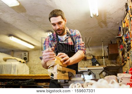 profession, carpentry, woodwork and people concept - carpenter working with plane and wood plank at workshop