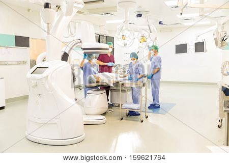 Wide angle view of a team of doctors preparing a patient for a cardiac procedure in a state of the art operating room. Endovascular equipment shown