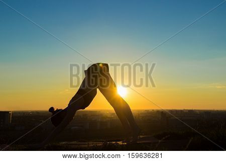 Silhouette of sporty woman doing Ashtanga yoga in the park at sunset. Sunset light, sun lens flares, golden hour. Freedom, health and yoga concept