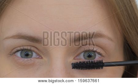 Close up shot. Beautiful young woman putting mascara and looking at camera. Beauty and makeup concept