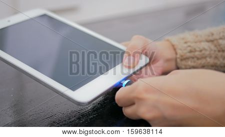 Woman's hand plugging black lightning charging cable into pc digital tablet - USB data cable connecting on modern gadget. Close up