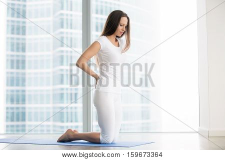 Young frustrated woman in studio trying to reduce stress, relieve aches and pains with yoga help, feeling backpain or unable to perform asanas, rehabilitation after spine trauma, beginner yoga fails