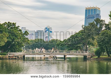 Bangkok, Thailand - December 23, 2015: People relax on boat in a city park. Pleasureboats on a lake in the heart of Bangkok - Lumphini Park. Business district cityscape with cloudy sky in the evening