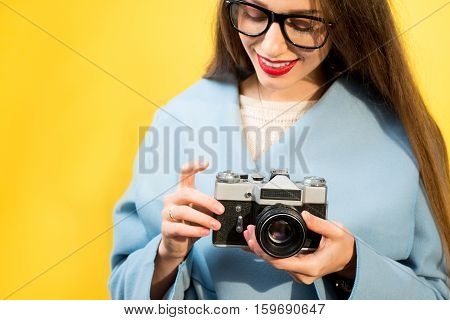 Stylish woman photographer with retro camera on the yellow wall background
