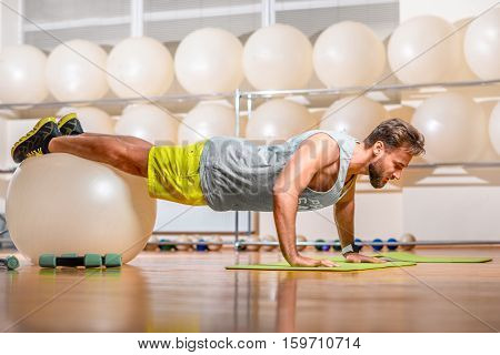Sports man making push-ups with fitball in the fitness room