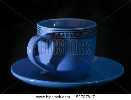 Cup and shadow on her in the form of a heart. The blue cup on a black background the handle casts a shadow in the form of heart