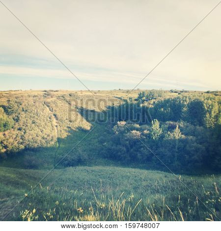Landscape with lush vegetation and sunshine on hills in autumn. Grey clouds and light blue sky over sunset orange colored hills in background. Thick forest trees and lush grass.Hills and valley.