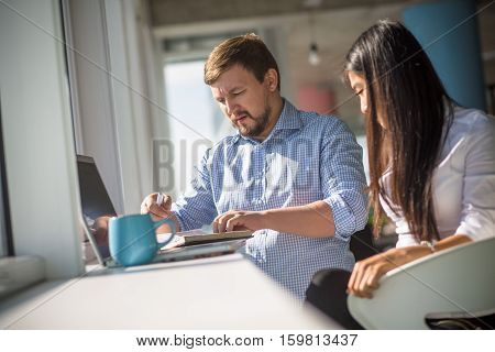 Businessman and businesswoman working on laptop compuer and with documentation in front of window in office interior. Business or freelance concept.