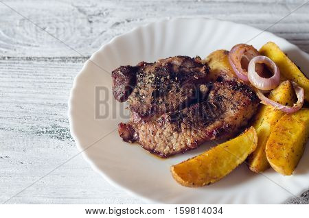 Grilled pork steaks with baked potatoes on plate