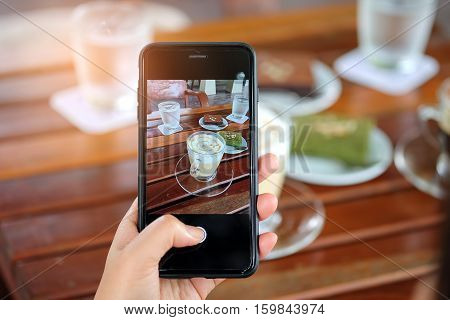 Smartphone in hand with latte coffee and cake on table.Photo latte coffee on diaplay.