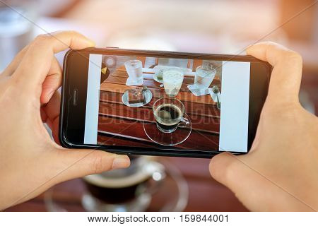 Smartphone in hand with coffee and cake on table.Photo coffee and cake on diaplay.
