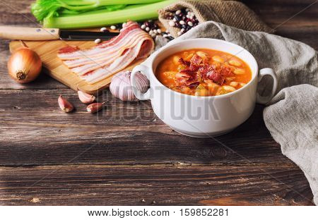 Homemade bean soup in white bowl on rustic wooden background with ingredients.