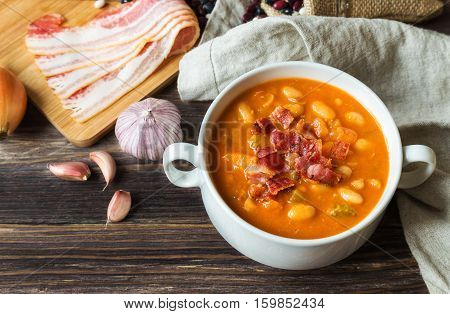 Homemade bean soup in white bowl on rustic wooden background with ingredients.