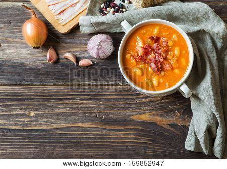 Homemade bean soup in white bowl on rustic wooden background with ingredients. Top view.