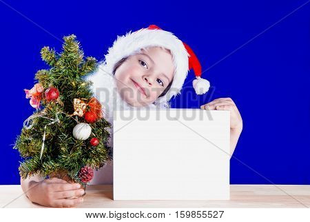 The charming little boy dressed as Santa Claus received Christmas gifts. Smiling and looking into the camera. Gift in a white box. On a blue background. Close-up.