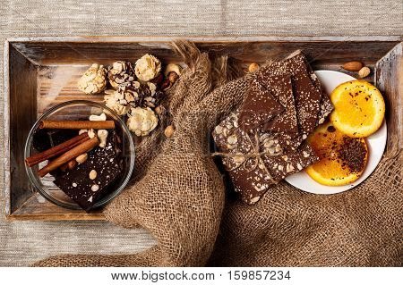 Chocolate candies cinnamon orange and nuts over sackcloth background. From above. Copy space.