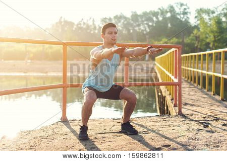 Fit man warming up doing squats stretching arms forward outdoors