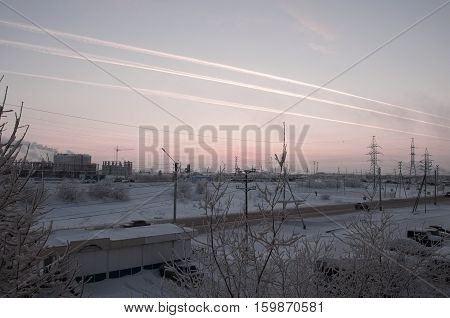 Pink sunset on the winter industrial street with prints in the sky after the airplane  View from window in the cold frosty evening. Road with cars
