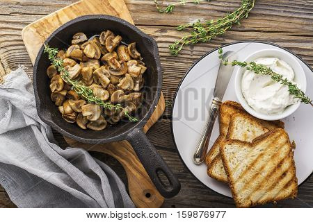 Fried mushrooms in a pan with a batch curd cheese on crispy toast for breakfast. Top view
