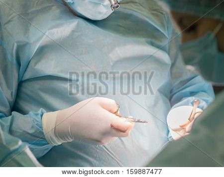 Close-up image of surgeon putting on stitches during cosmetic surgery in hospital operating room. Doctor holding forceps stitching the patient up. Breast augmentation enlargement enhancement