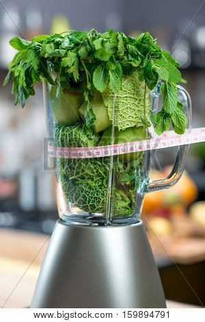 Close up view on the blender full of green fruits and vegetables ready to mix with meter in the kitchen. Healthy vegetarian diet for weight loss and detox