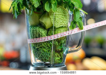 Close up view on the blender full of green fruits and vegetables ready to mix with meter in the kitchen. Healthy vegetarian diet for weight loss and detox