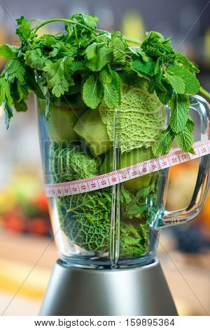 Close up view on the blender full of green fruits and vegetables ready to mix with meter in the kitchen. Healthy vegetarian diet for weight loss and detox