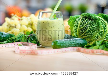 Glass with smoothie with green vegetables on the table in the kitchen. Healthy vegetarian diet for weight loss and detox
