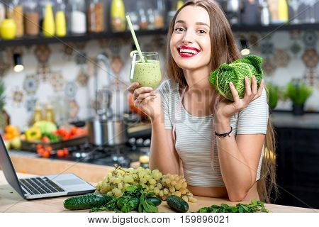 Portrait of young smiling woman with green smoothie in the kitchen at home. Healthy vegetarian diet for weight loss and detox