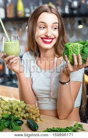 Portrait of young smiling woman with green smoothie in the kitchen at home. Healthy vegetarian diet for weight loss and detox