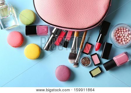 Makeup products with cosmetic bag and macaroons on blue background