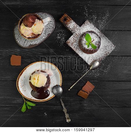 Chocolate lava cake (Molten) with ice cream on plate. Balls of ice cream in cup. Chocolate lava cake (Molten) with mint on board. Pieces of chocolate. Dark black wooden background. Top view blank space.