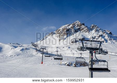 Ski lift in mountains at winter. Alpine winter mountain landscape. French Alps covered with snow in sunny day. Val-d'Isere, Alps, France