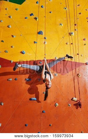 Love extreme. Active young delighted woman making a trick on a climbing wall while training and wearing sportswear and special equipment.
