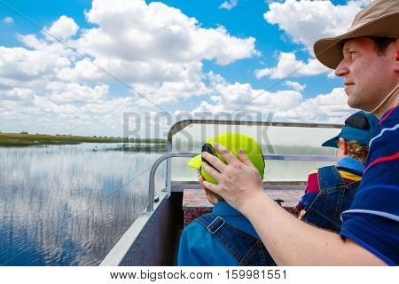 Little kid boy and father making air boat tour in Florida wetland swamp at Everglades National Park in USA. Family, dad and child discovering wild nature and animals. Family having fun.