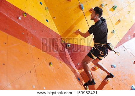 Pleasant times. Handsome young delighted man training hard in climbing gym while using equipment and climbing up the wall.