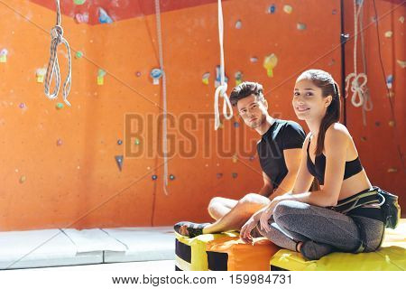 Do it together. Delighted young active couple sittiing in a climbing gym after training and climbing up the wall.