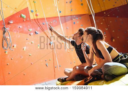 Joyful activity. Happy young active couple sittiing in a climbing gym after training and climbing up the wall.