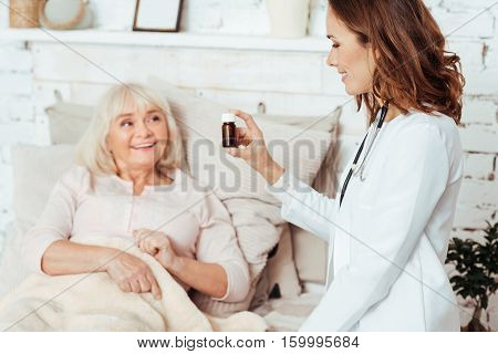 One pill per day. Positive ill aged woman lying in bed wile professioanl doctor vising her and giving remedy