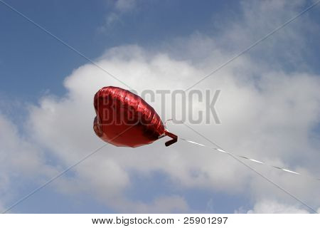 Czerwony Mylar centrum helu balon unosi się przeciw błękitne niebo, białe chmury puszyste