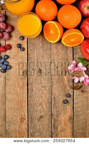 Orange Juice, Fresh Oranges, Apples, Grapes, Raspberries, Blueberries And Spring Flowers On A Wooden