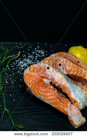 Slices Of Red Fish Salmon On Trout With Lemon, Dill, Pink And White Salt, On Black Wooden Background