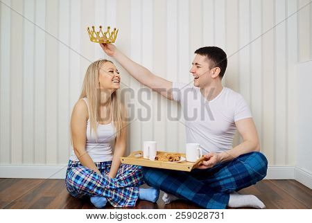A Happy Couple In Pajamas Sit On The Floor A Striped Wall Backgr