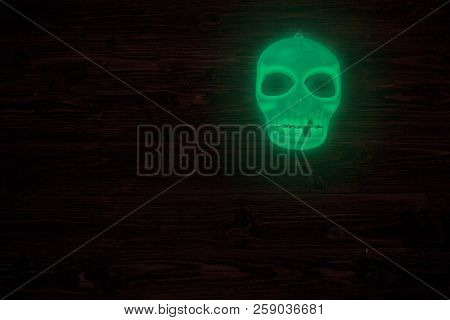 Halloween Glowing Phosphoric Human Skull Over Wooden Table Background. Neon Light